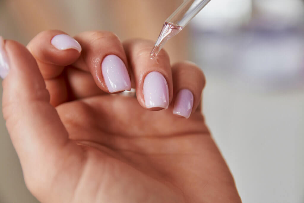 Óleo sendo aplicado nas unhas pintadas de rosa claro