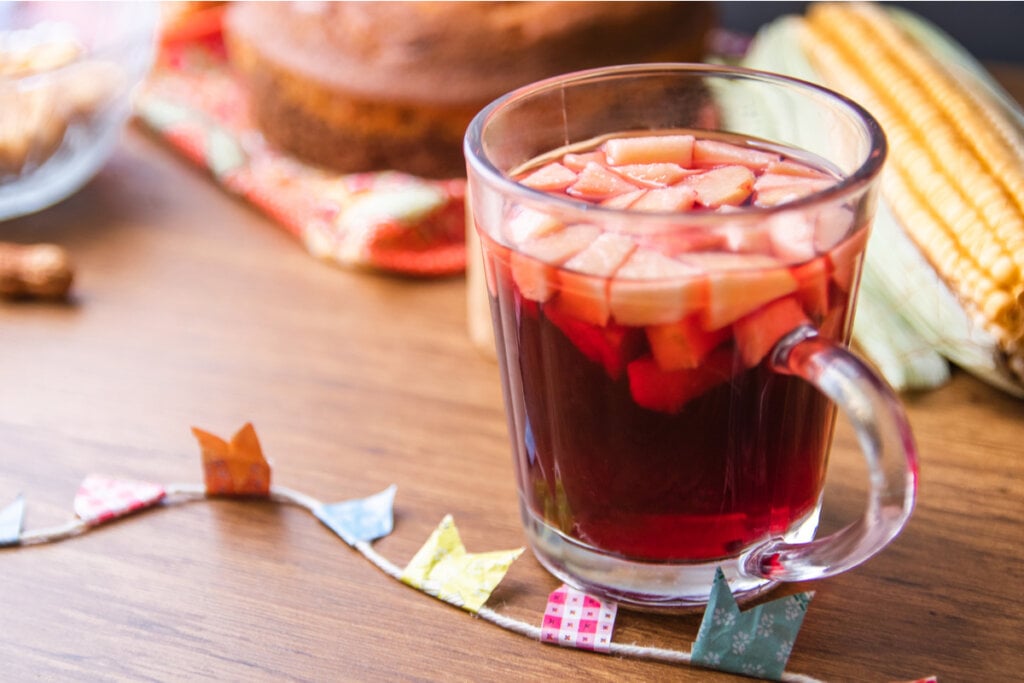 Vinho quente com maçã em caneca de vidro e decoração junina em volta