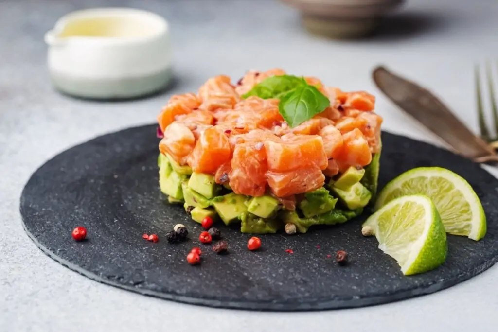 Tartar de salmão com abacate em um prato escuro em cima de uma mesa