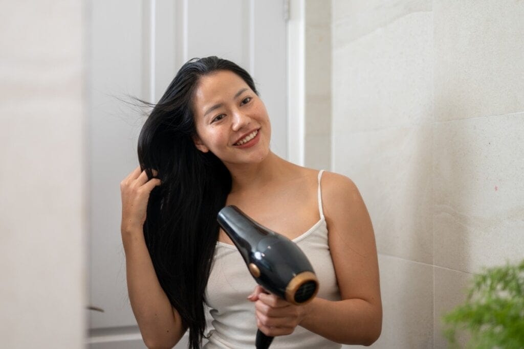 Mulher com cabelo preto, liso e longo em um banheiro secando o cabelo