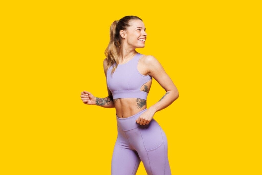Mulher usando roupa de academia e olhando para o lado em frente a um fundo amarelo