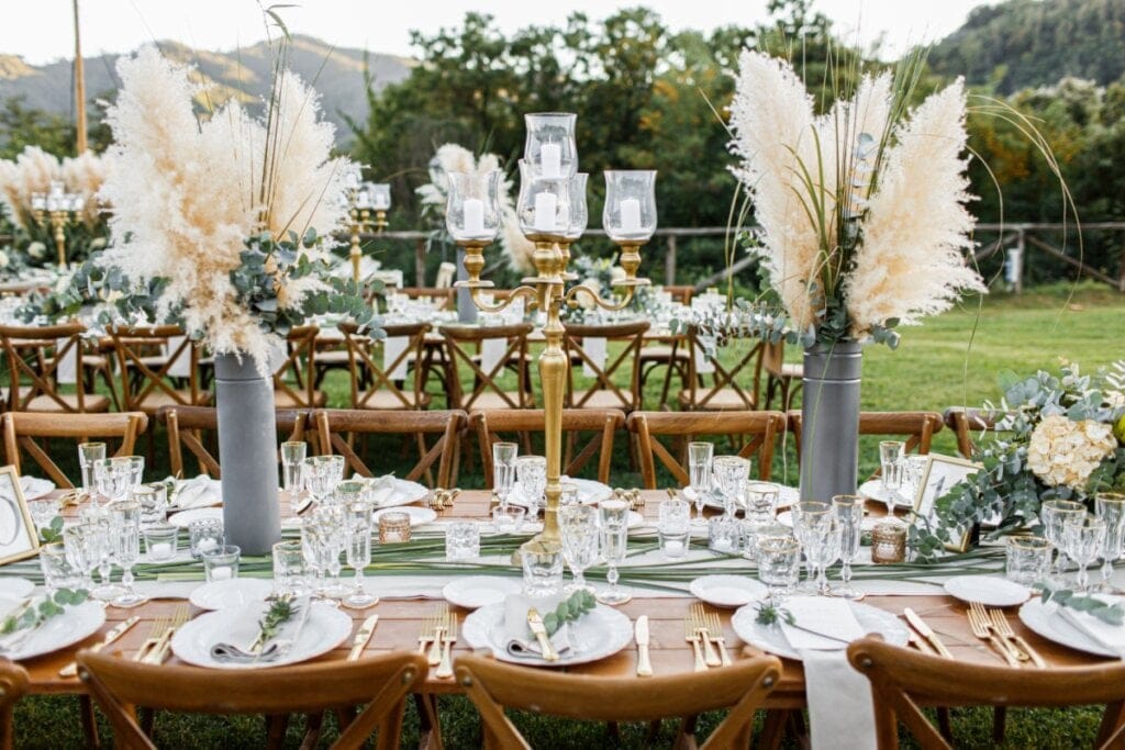 Decoração de casamento ao ar livre com arranjos de pampas, candelabros dourados e mesa posta com detalhes em dourado