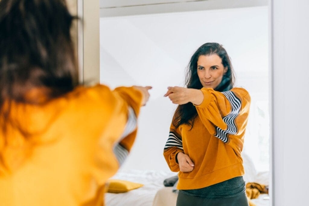Mulher em frente a um espelho sorrindo e apontando para si 