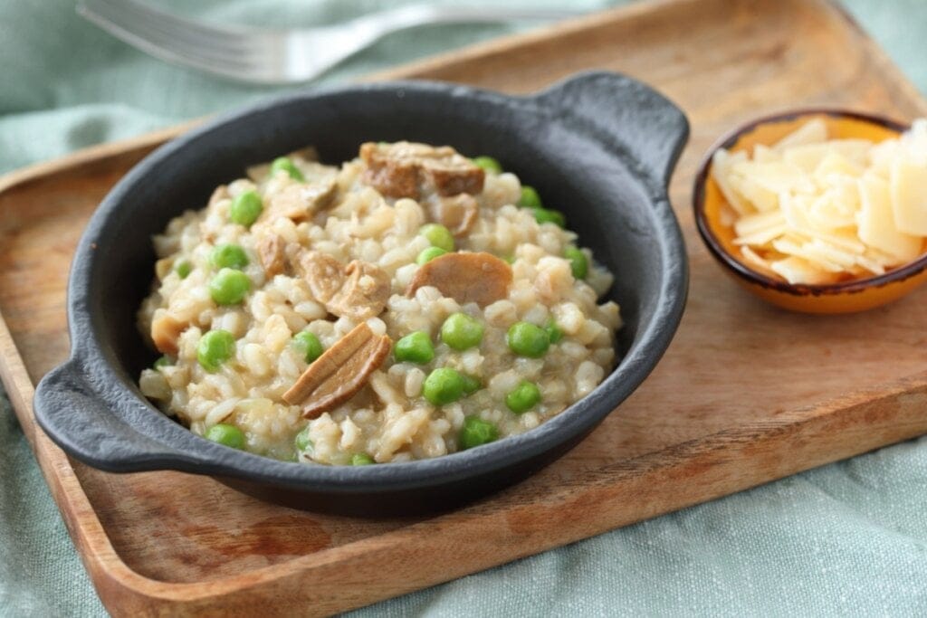 Panela preta com risoto de cogumelo com ervilha em cima de uma tábua de madeira