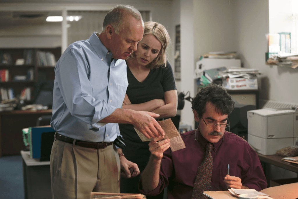 Três jornalistas analisando recortes de jornal em uma redação, representando uma das investigações no filme Spotlight – Segredos Revelados