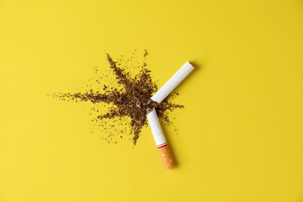 Cigarro quebrado ao meio com o conteúdo espalhado em um fundo amarelo