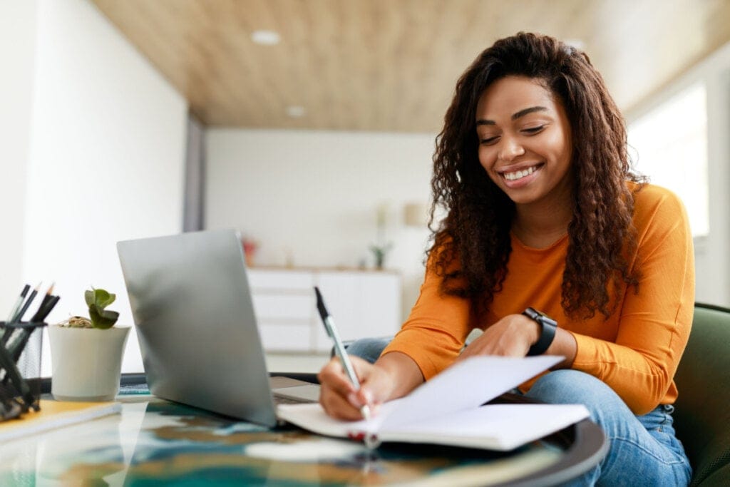 Mulher em frente ao notebook anotando informações em um caderno