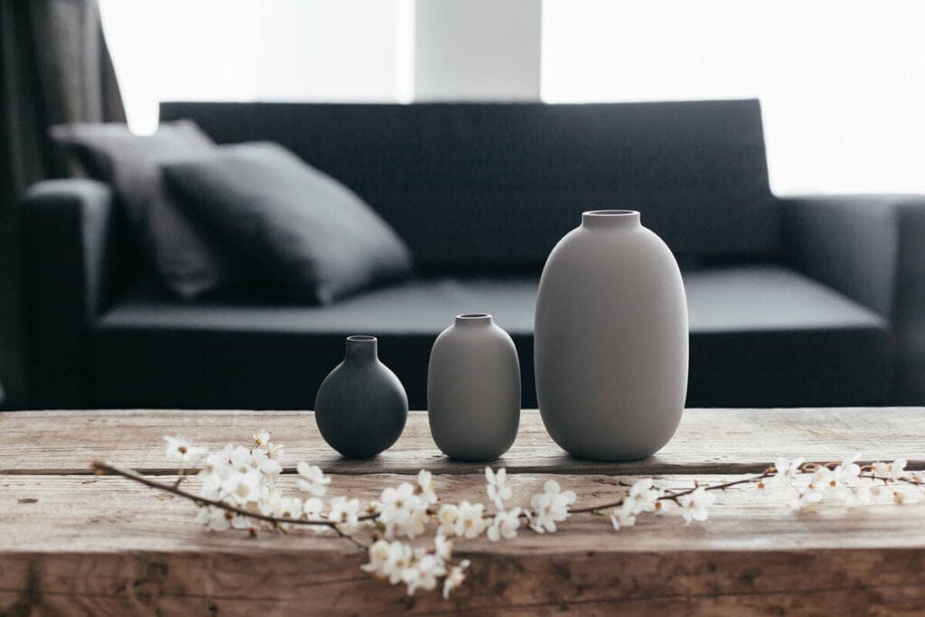 Três vasos de planta cinzas em cima de uma mesa com flores