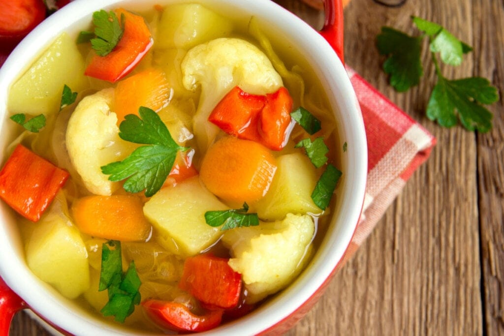 Sopa antioxidante, com cenoura, batata, pimentão, tomate e folhas verdes picadas em cima 