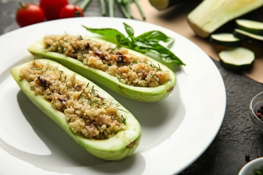 Duas abobrinhas recheadas com quinoa em cima de um prato branco