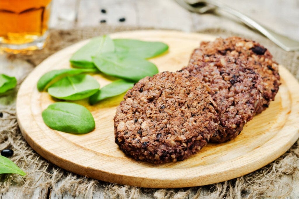 Hambúrguer vegetariano de feijão-preto em tábua com folhas de rúcula 