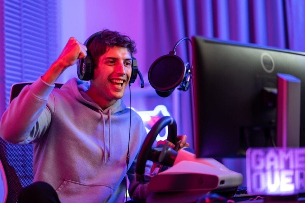 homem gamer de fone de ouvido, comemorando e segurando volante de videogame de frente para a TV