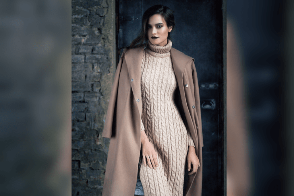 Mulher de vestido longo de tricô e casaco sobre os ombros em ambiente com tijolos
