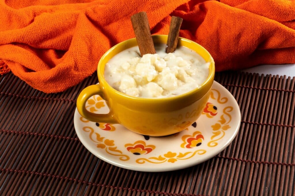 Xícara amarela com canjica e duas canelas em paus