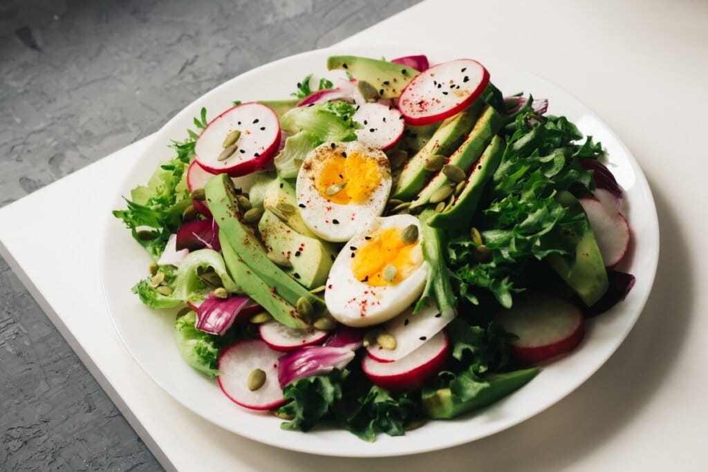 Prato branco com folhas verdes, rabanete, abacate, ovos, sementes de abóbora e gergelim preto