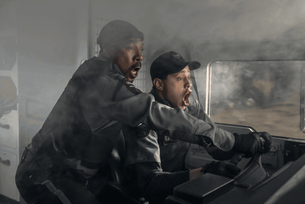 Dois homens usando uniformes pretos gritando dentro de um carro que está cheio de fumaça dentro