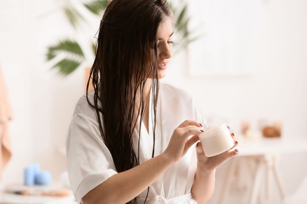 Mulher com o cabelo liso longo, cuidando do cabelo após o banho, usando um roupão branco 