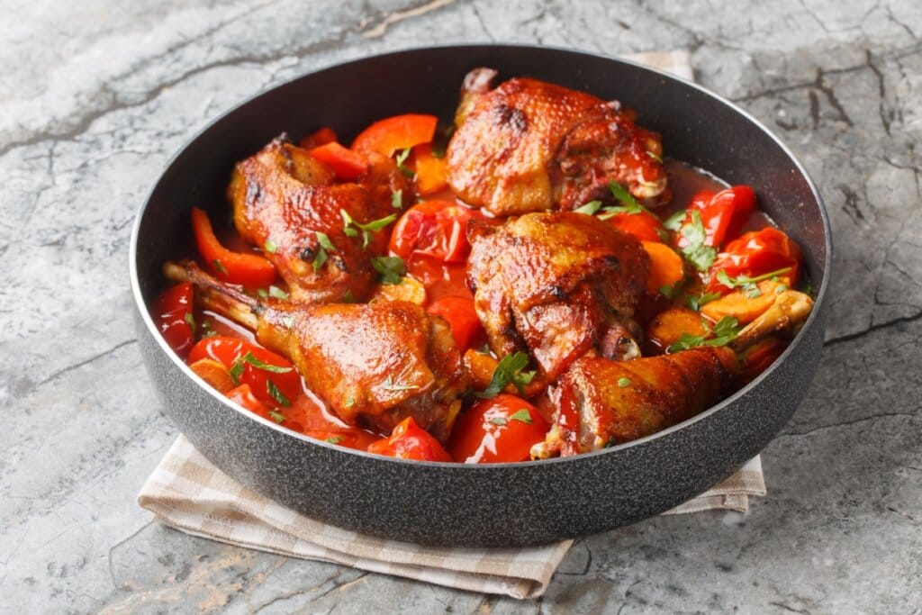 Panela com coxas e sobrecoxas de frango douradas ensopadas em molho de tomate com pimentão e cenoura