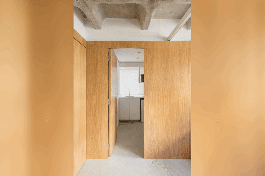 Porta camuflada em painel de madeira clara conduzindo a outro ambiente em apartamento contemporâneo