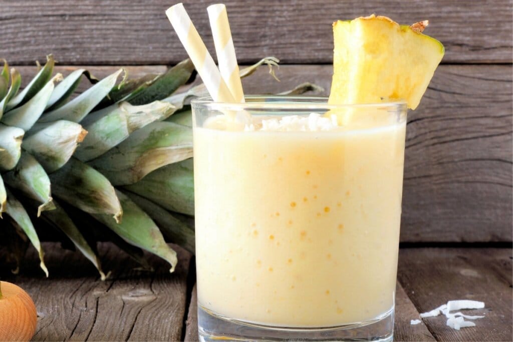 Copo de vidro com vitamian de abacaxi decorado com um pedaço de abacaxi 