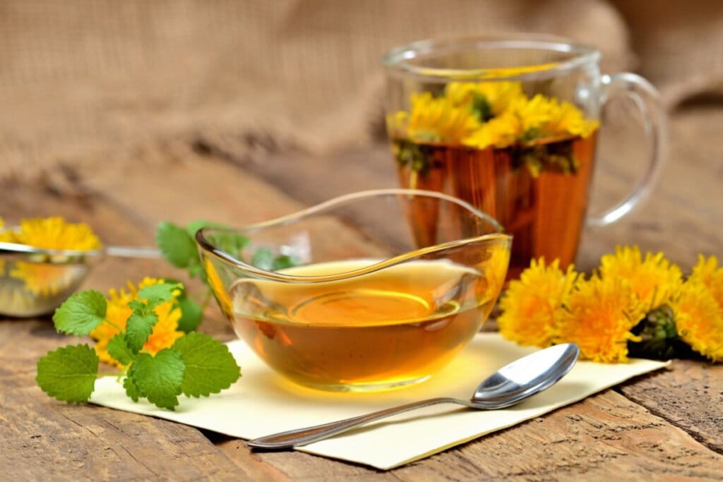 Chá de dente-de-leão com hortelã e limão servido em xícara de vidro em cima de mesa de madeira