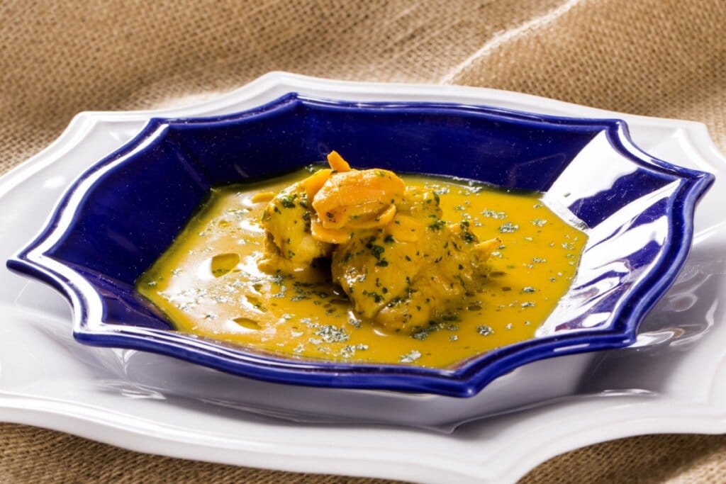 Frango ao molho de pequi servido em prato azul de cerâmica em cima de prato branco de cerâmica em cima de mesa de madeira