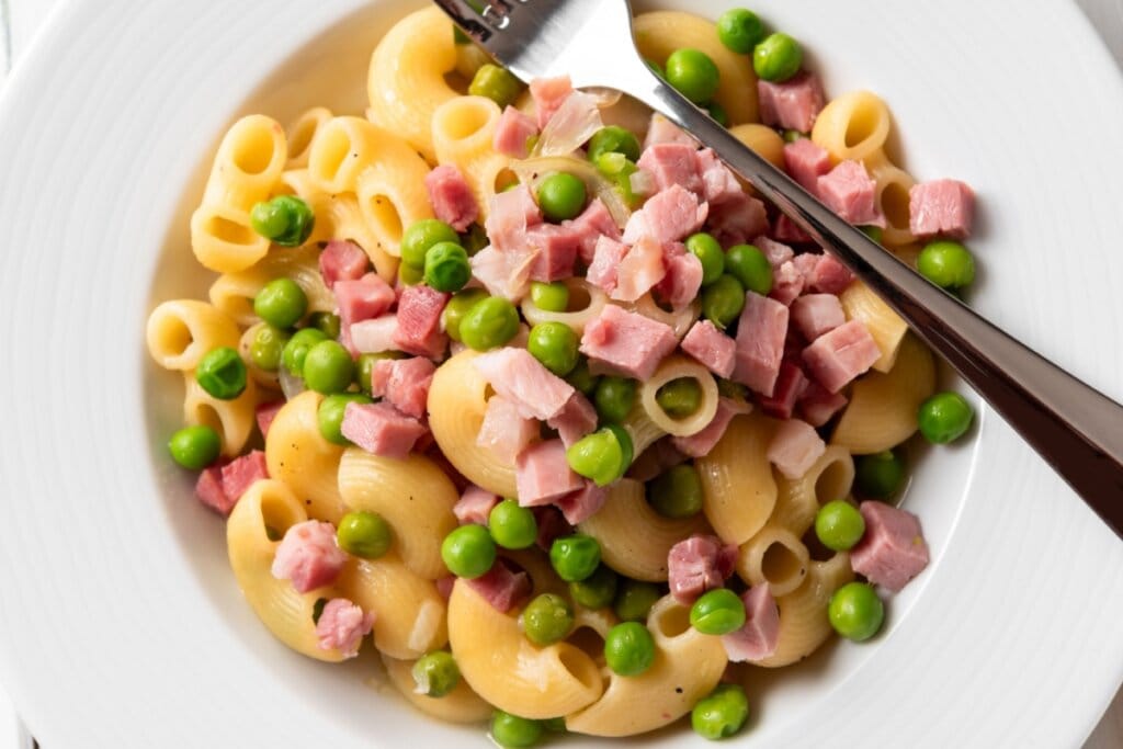 Prato branco com macarrão com presunto e ervilha