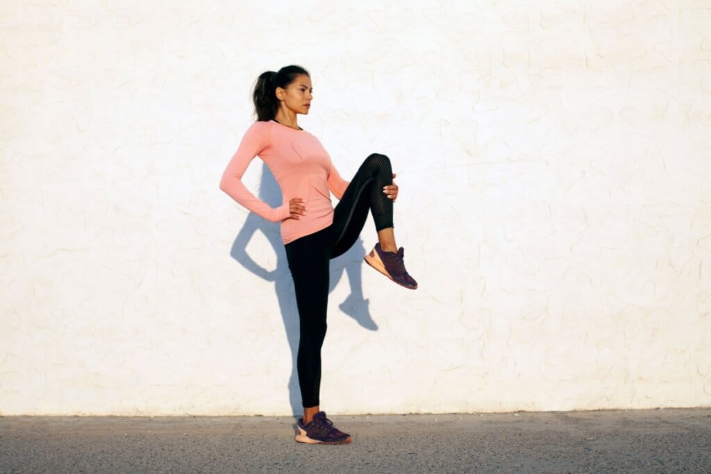 Mulher em pé com uma das pernas levantada em direção ao tórax 