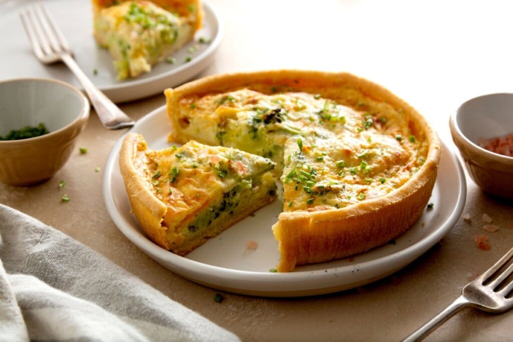Quiche de brócolis em cima de um prato branco com um pedaço cortado
