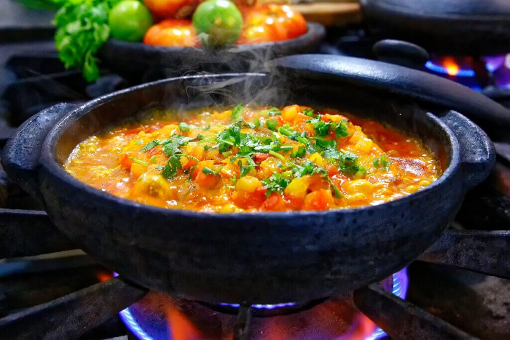 Moqueca na panela preta em cima do fogão com cebolinha