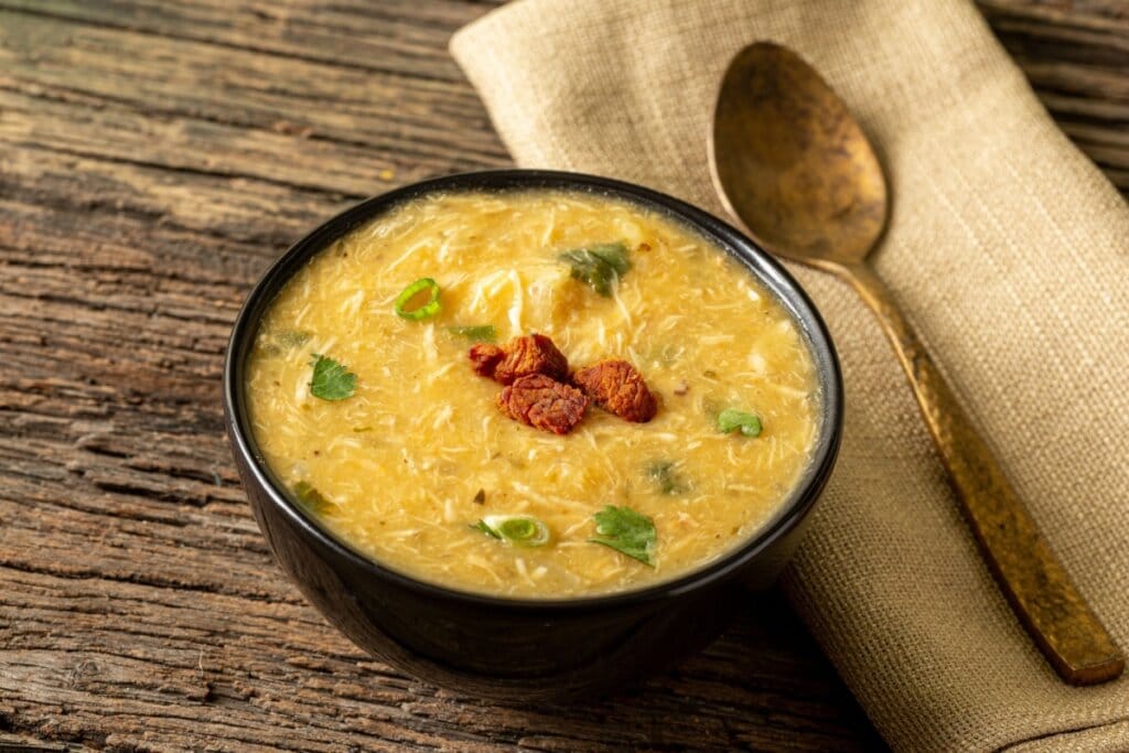 recipiente preto com caldo de frango com salsinha e colher ao lado