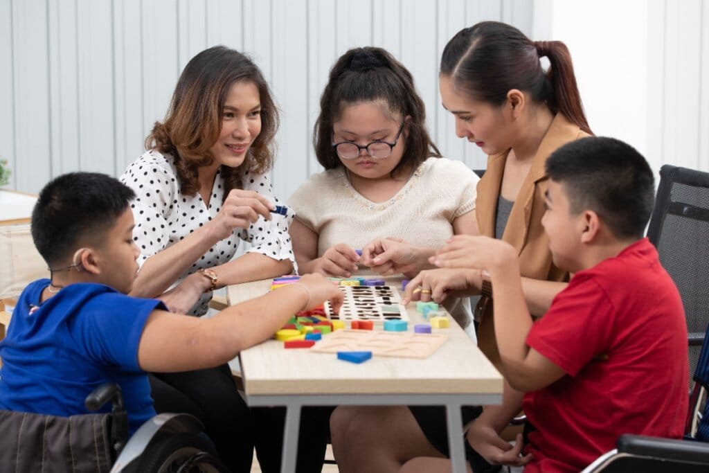 Professora e assistente acompanhando crianças com deficiência em uma atividade com peças coloridas em sala de aula