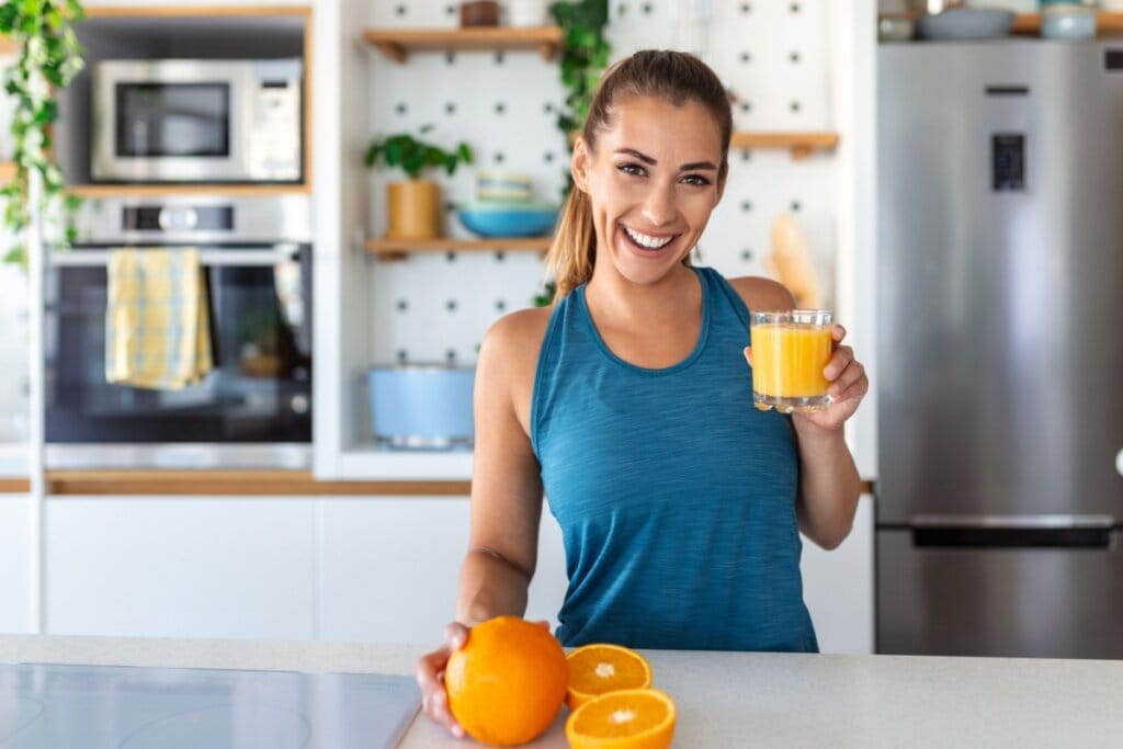 Mulher em uma cozinha segurando um copo com suco de laranja