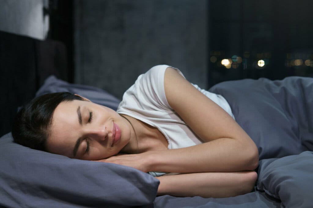 Mulher deitada em uma cama com travesseiro e cobertor cinza. ela está dormindo