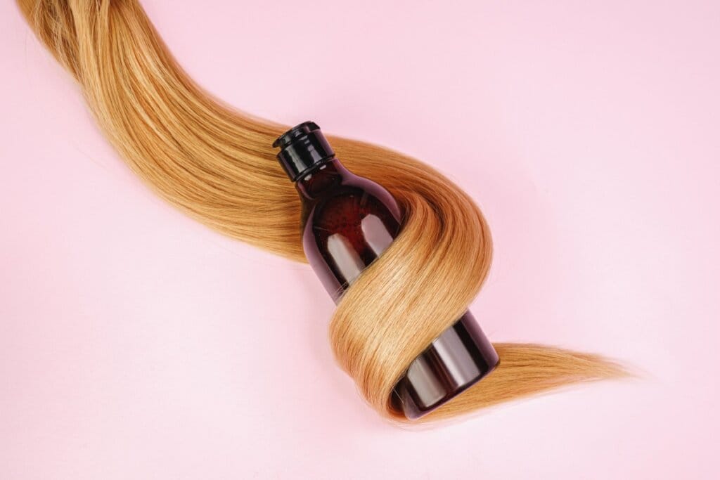 Vidro de shampoo enrolado em cabelo ruivo em fundo rosa