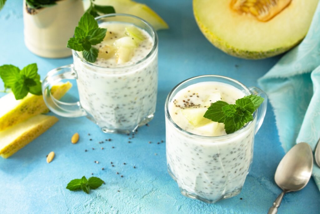 Copos de vitamina de melão com chia e folhas de hortelã ao lado de pedaços de melão fresco e colher