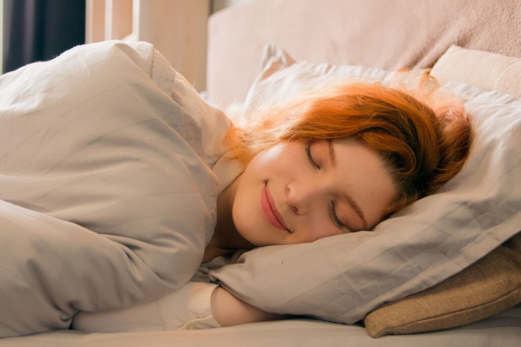Mulher ruiva dormindo em cama com travesseiro e cobertor cinza