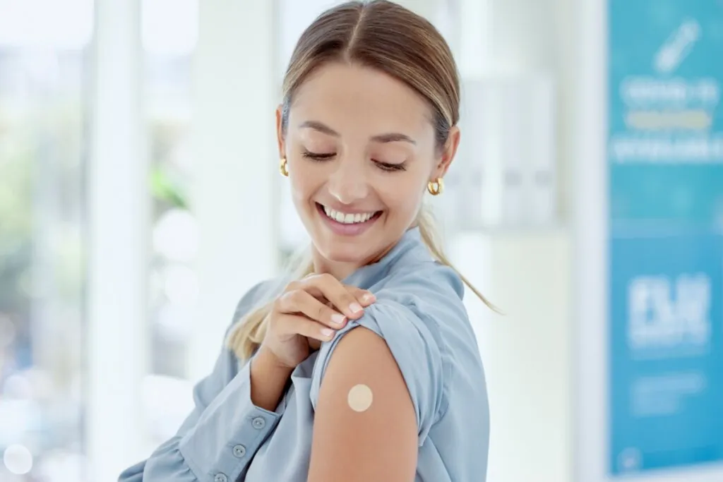 Mulher sorrindo, levantando manga de blusa azul e olhando para curativo de vacina no braço