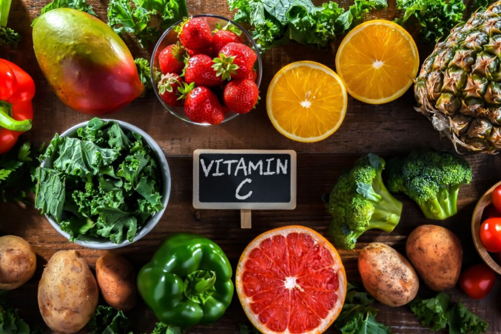 Alimentos ricos em vitamina C espalhados ao lado de placa escrito vitamin c em cima de bancada como laranja, morango, abacaxi e outros