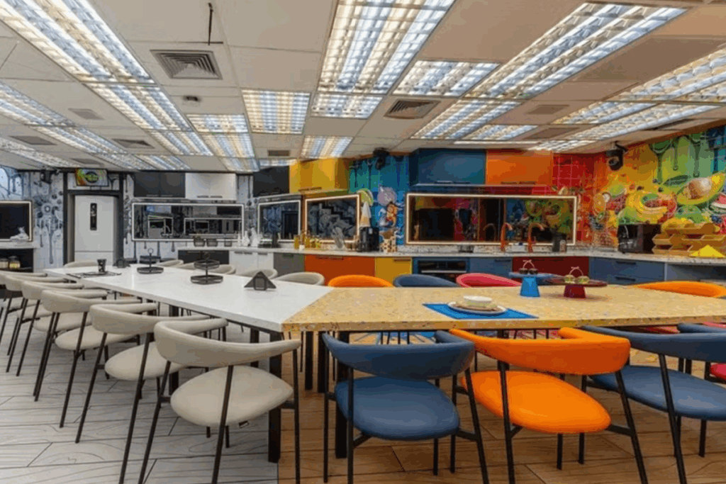 Cozinha da casa do BBB 26 com bancadas amplas, mesas coletivas, cadeiras coloridas e divisão entre áreas VIP e Xepa