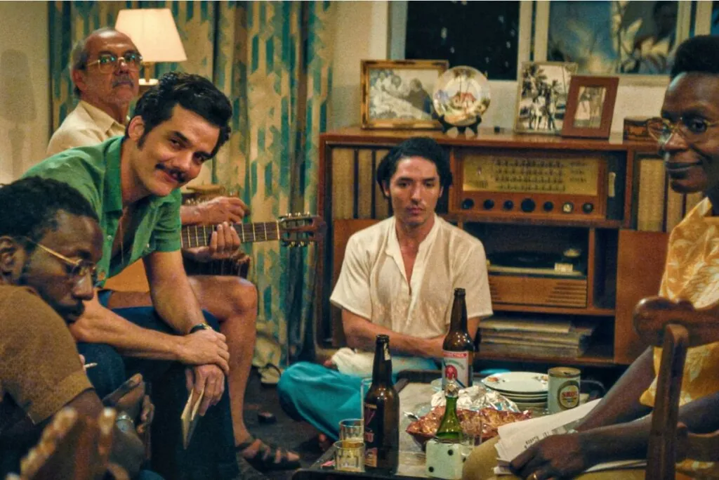Quatro homens e uma mulher, sentados em uma sala de estar conversando