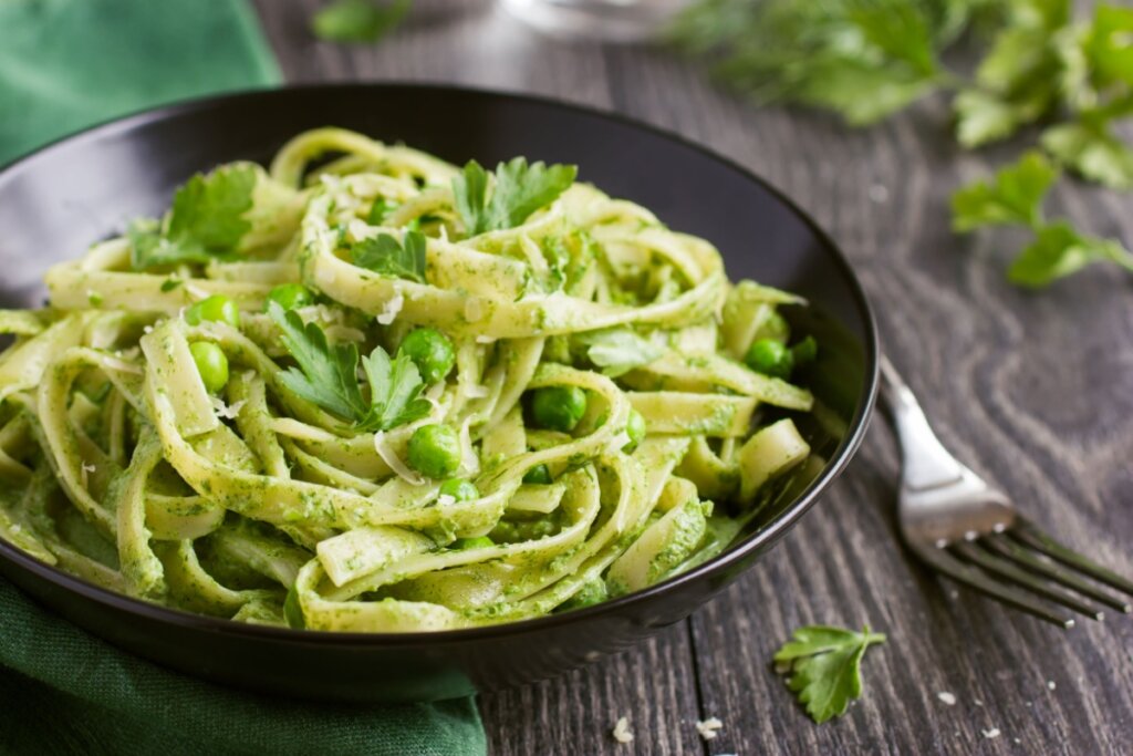 prato preto com macarrão com molho verde, ervilha e salsinha em superfície de madeira