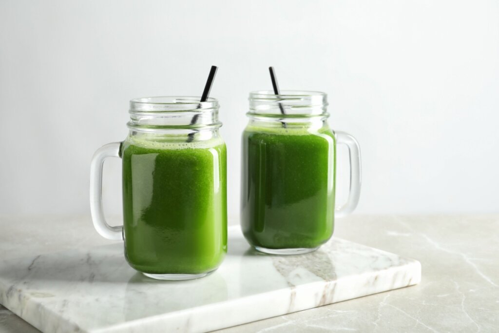 Dois copos de vidro com suco verde e canudo preto em cima de bancada de mármore
