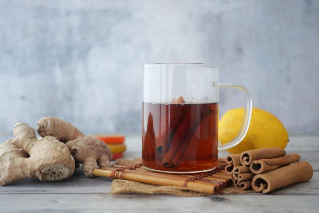 Chá de gengibre com limão-siciliano e canela em xícara transparente com especiarias ao lado.