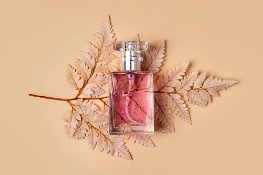 Vidro de perfume com perfume rosa em cima de folha de outono em fundo bege claro