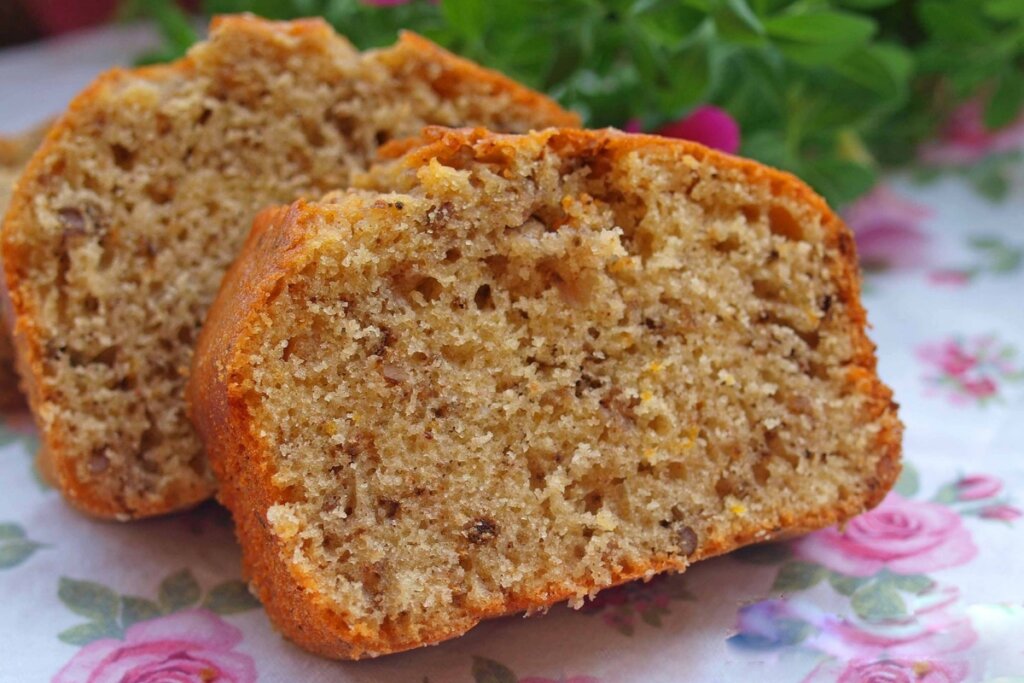 Dois pedaços de bolo em cima de uma mesa com toalha branca com flores rosa 