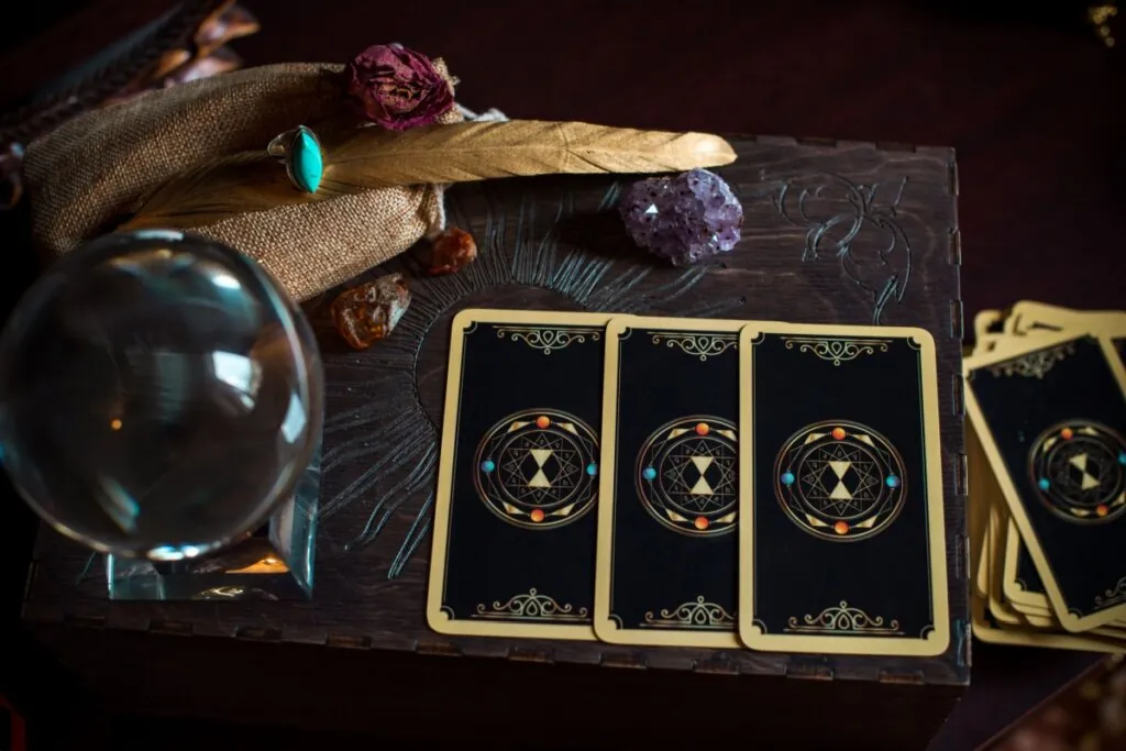 Imagem de cartas de tarot ao lado de pedras, um anel e uma bola de cristal