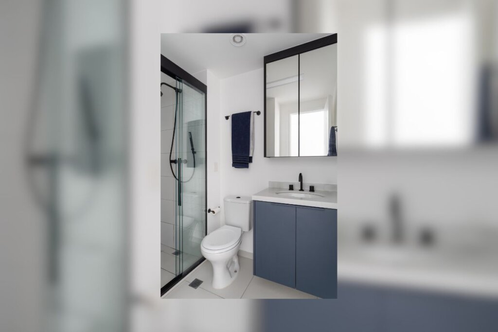 Banheiro com box em três partes, paredes branca e móveis azuis 