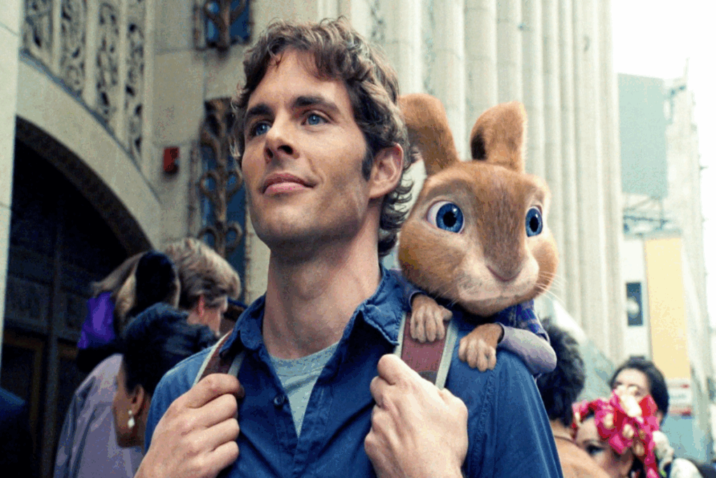 Homem com cabelo curto, usando camiseta azul-clara e camisa azul-escura segurando alças de mochila e com um coelho marrom encostado em seu ombro