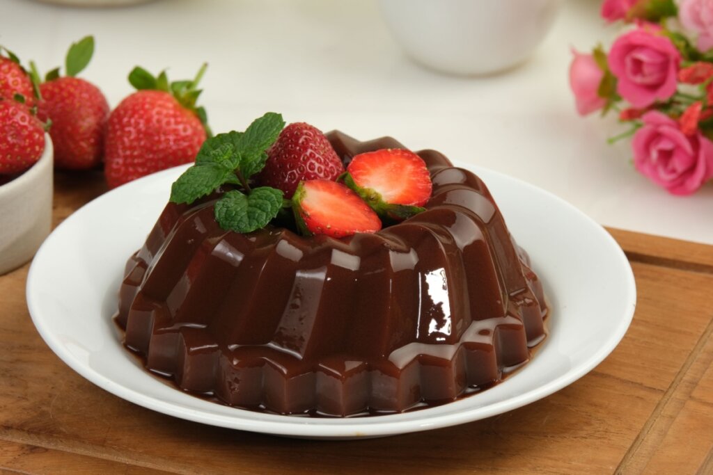 Pudim de chocolate servido em prato branco de porcelana em cima de mesa de madeira